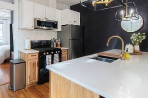 A modern kitchen with white cabinets, a black refrigerator, a stainless steel microwave, and a built-in oven. - Cozy 1BD Rowhome w/Private Terrace: Wash Park (Denver)