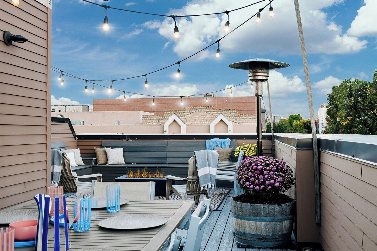 A rooftop patio with outdoor furniture, string lights, and a fire feature.