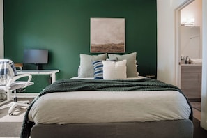 Ein Schlafzimmer mit Bett, Kissen, einem Schreibtisch mit Computer und einer grünen Wand.