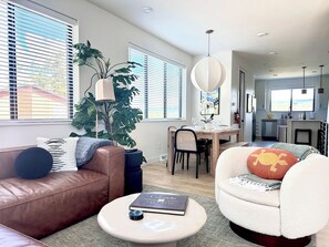 A modern living room with a brown leather sofa, a white armchair, and a dining area in the background. - Mountain Modern Retreat w Hot Tub 3Bed Winter Park (Fraser)