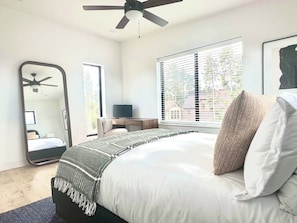 A bedroom with a bed, a ceiling fan, a large mirror, a window with blinds, and a desk with a chair. - Mountain Modern Retreat w Hot Tub 3Bed Winter Park (Fraser)