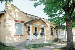 Une maison à deux étages avec un porche, des marches menant à la porte d’entrée et un arbre au premier plan.