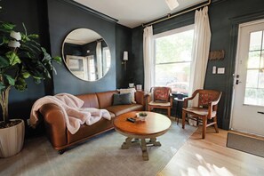 Un salon avec un canapé en cuir marron, une table basse ronde, une plante en pot et un grand miroir au mur.