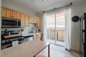 A kitchen with wooden cabinets, a stainless steel microwave, a gas stove, and a large window with a view of a wooden fence. - Boutique 1BD Townhome w/Great Patio in Wash Park (Denver)