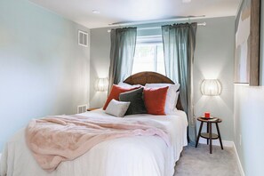 A bedroom with a bed, a bedside table with a lamp, and a window with curtains. - Cottage Escape 1 BD w/Large Yard: Sloans Lake (Denver)