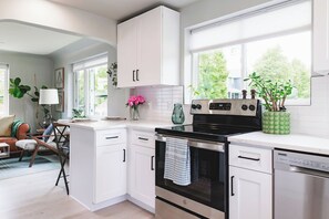 A modern kitchen with white cabinetry, a black stove, and a dishwasher. There is a window with a view of greenery outside. - Cottage Escape 1 BD w/Large Yard: Sloans Lake (Denver)