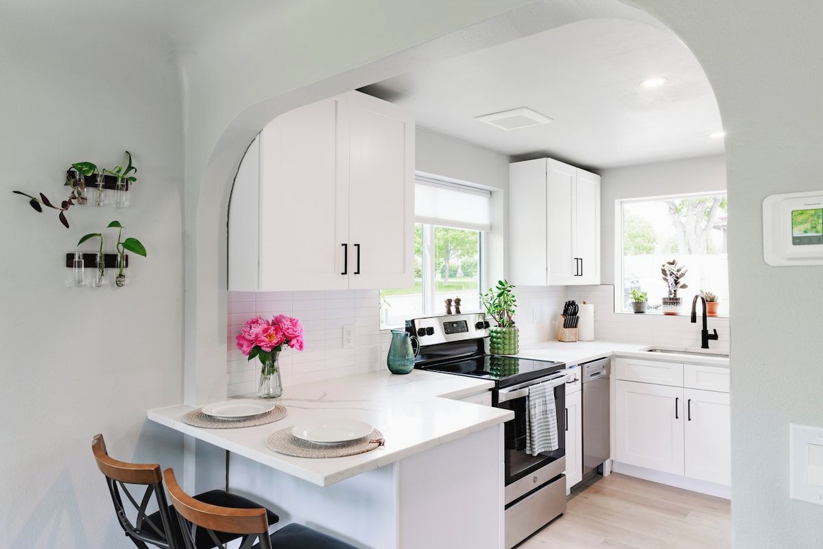 A modern kitchen with white cabinetry, a central island, and a dining area with chairs.