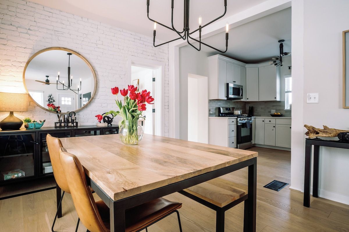 A modern kitchen with white cabinets, a wooden dining table, and a large mirror.