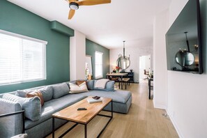 A modern living room with a grey sofa, wooden coffee table, and a dining area in the background. - Home Away from Home w/Sauna 4BD|2BA | Berkley (Denver)