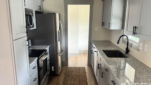 A modern kitchen with grey cabinets, stainless steel appliances, a granite countertop, and a wooden floor.