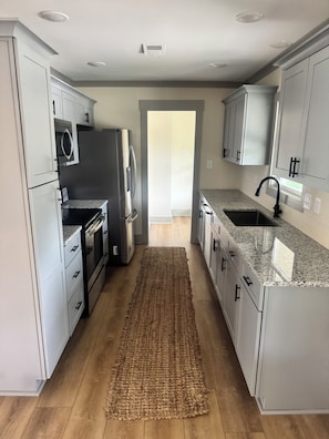 A modern kitchen with grey cabinets, stainless steel appliances, a granite countertop, and a wooden floor.