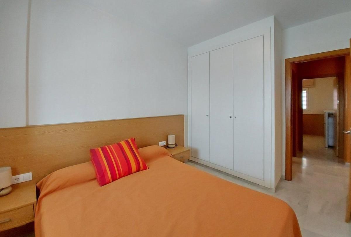 Een hotelkamer met een bed, nachtkastje, garderobe en een deur naar een andere kamer.