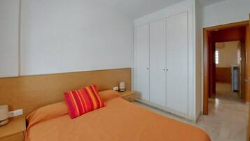 Een hotelkamer met een bed, nachtkastje, garderobe en een deur naar een andere kamer.
