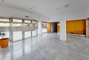 A spacious lobby with a clear glass door marked 'SALIDA,' a potted plant, and a wooden bench.