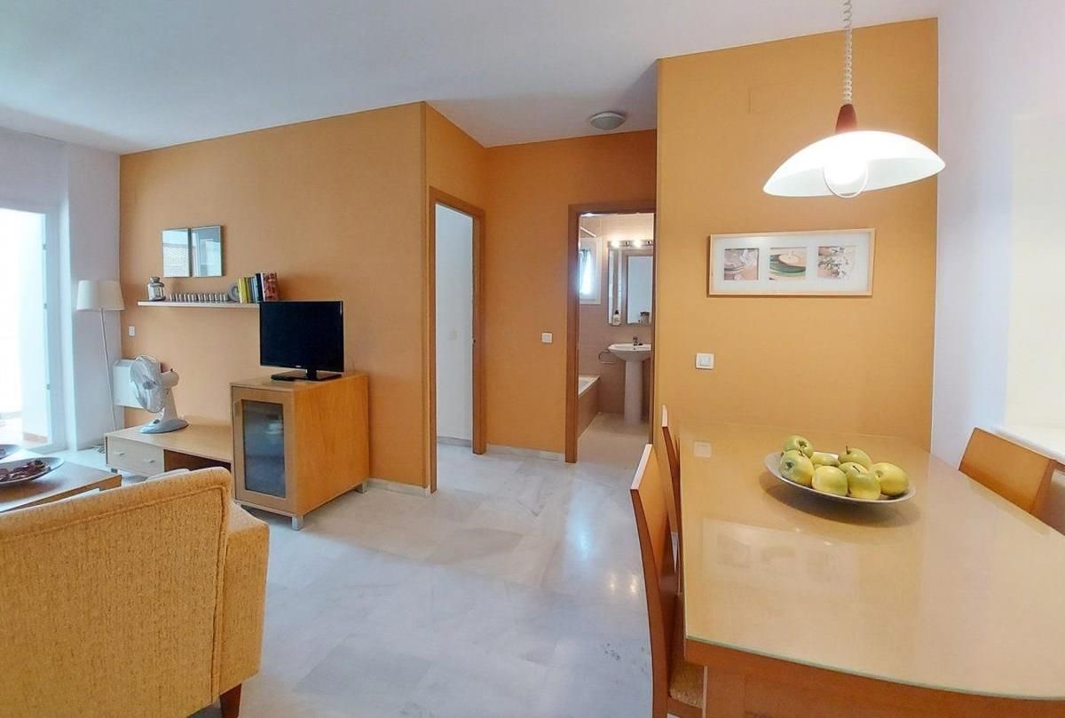 Una sala moderna con un televisor de pantalla plana, una mesa de comedor con sillas y una cocina visible al fondo.