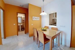 Een eethoek met een tafel, stoelen, een hanglamp en uitzicht op een keuken.