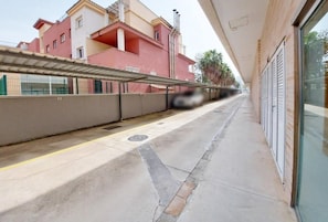 A corridor with a covered walkway, a building with balconies, and a clear sky.
