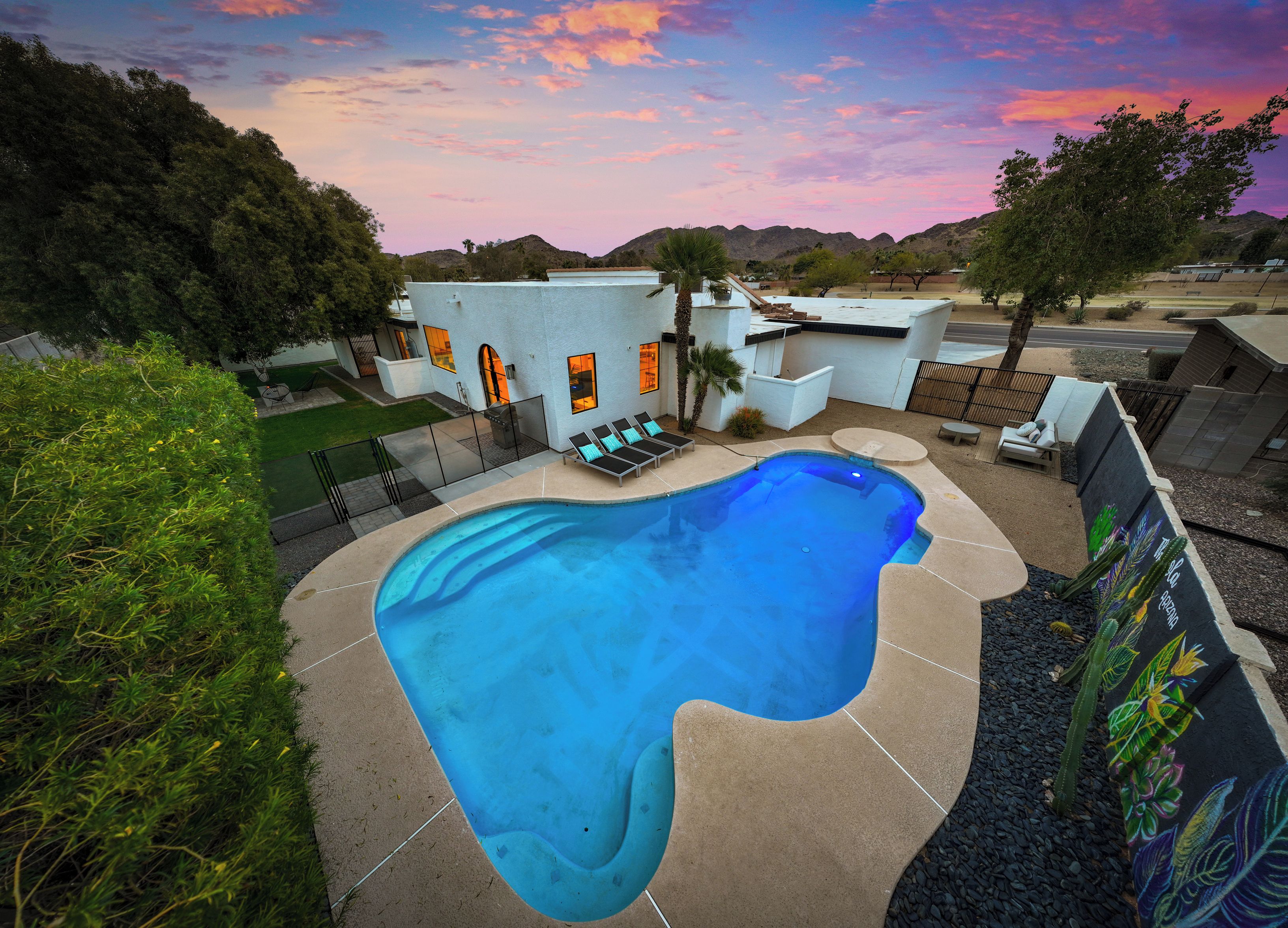A swimming pool with a unique shape, surrounded by a patio area with lounge chairs and a small deck.
