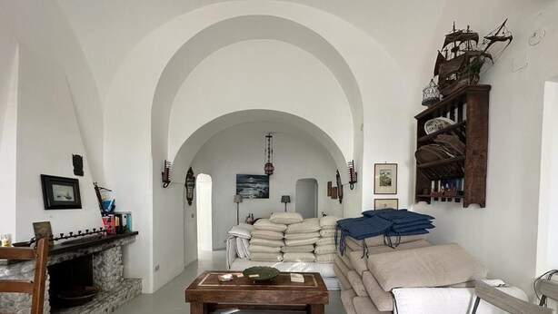 A room with a fireplace, a sofa, a coffee table, and a wooden shelf with decorative items. - TORRE SARACENA. Villa in Capri (M. Piccola) with beach access and a large terrace (Campania)