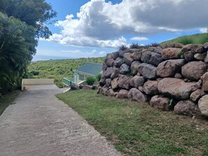 Un camí que condueix a una casa amb una paret de pedra a la dreta i una vista de paisatge verd a la distància.