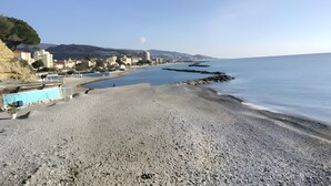 Ein Strand mit Kiesufer, einem klaren Himmel und Gebäuden im Hintergrund.