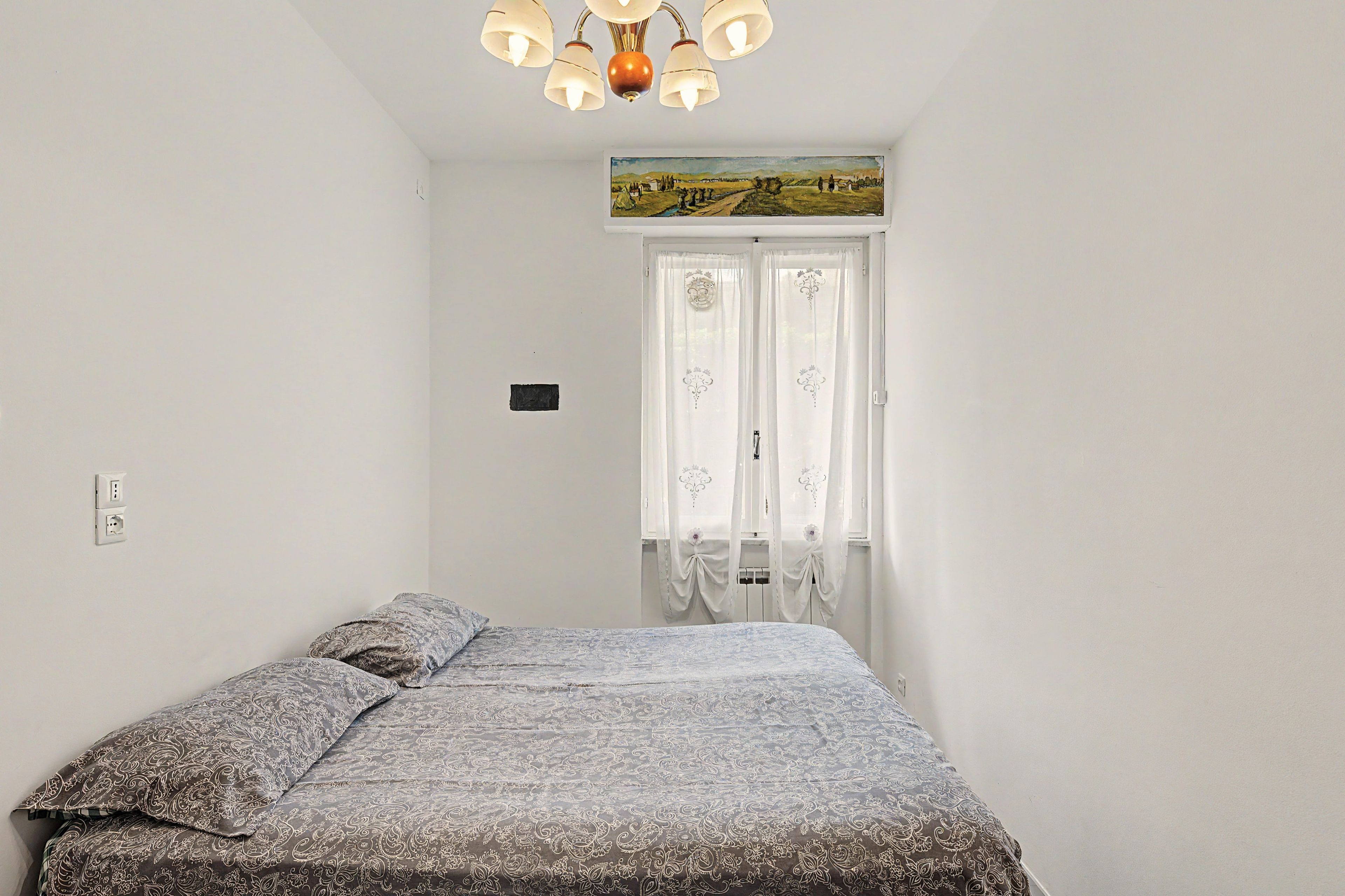 Een slaapkamer met een bed, een schilderij boven de deur en een kroonluchter.