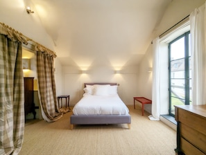 Ein Schlafzimmer mit einem Bett, einem kleinen Tisch, einem Nachttisch, einem Fenster mit Vorhängen und einer Wandleuchte.