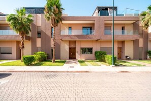 A multi-story building with a flat roof, a central entrance, and a paved walkway leading to it. - Villa Palm Atlas | Piscine Chauffé | proche centre (Marrakesh)