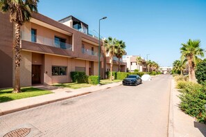 A residential street with modern apartment buildings, palm trees, and a parked car. - Villa Palm Atlas | Piscine Chauffé | proche centre (Marrakesh)