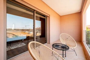 A balcony with two wicker chairs and a small table, a glass door leading outside, and a view of a construction site. - Villa Palm Atlas | Piscine Chauffé | proche centre (Marrakesh)