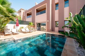 A modern building with a swimming pool, lounge chairs, and tropical plants. - Villa Palm Atlas | Piscine Chauffé | proche centre (Marrakesh)