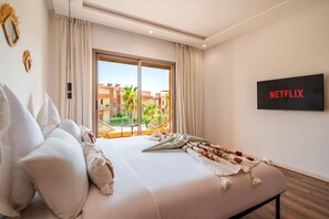 A hotel room with a large bed, a balcony with a view of buildings, and a TV screen displaying 'NETFLIX'. - Villa Palm Atlas | Piscine Chauffé | proche centre (Marrakesh)