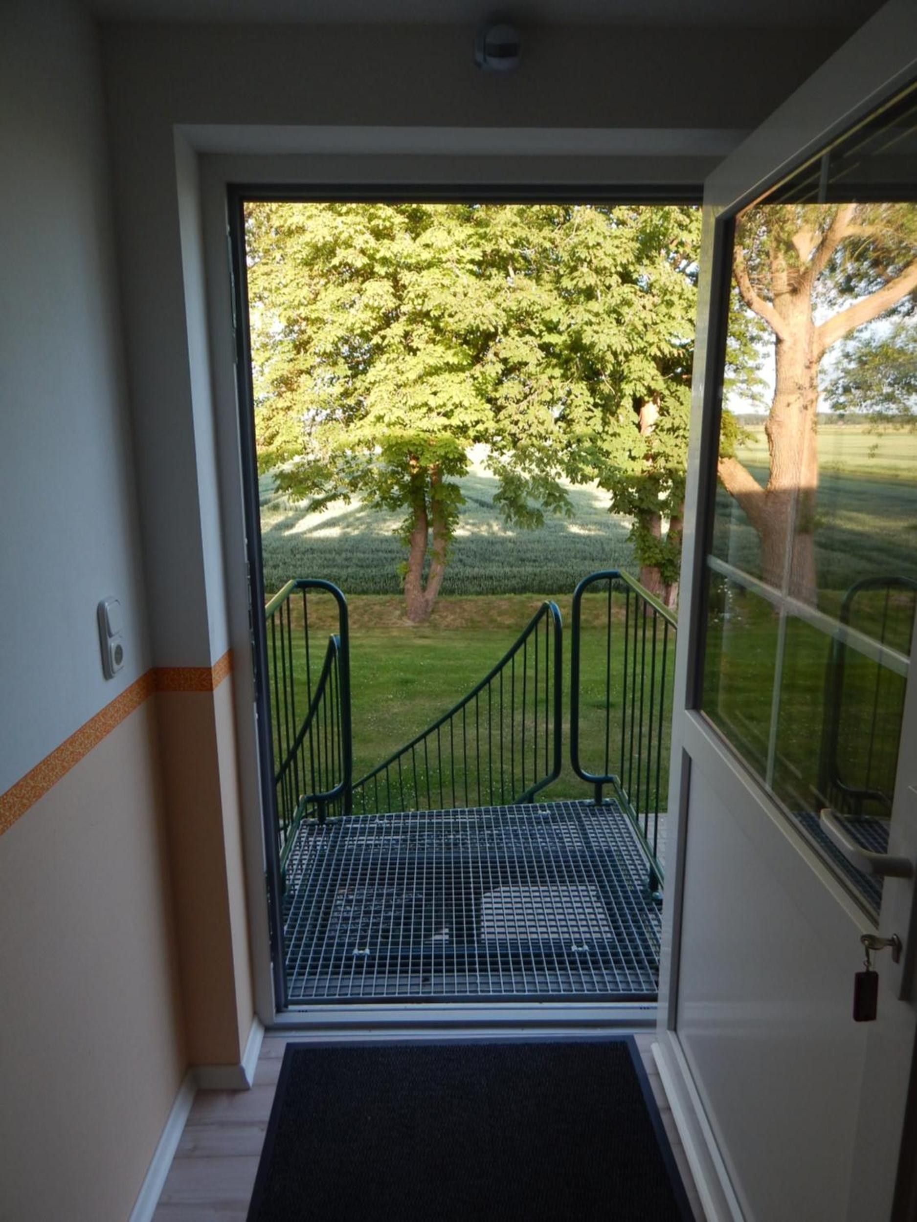 Puerta que da a un espacio al aire libre cubierto, con una escalera metálica y vistas a un césped bordeado de árboles.