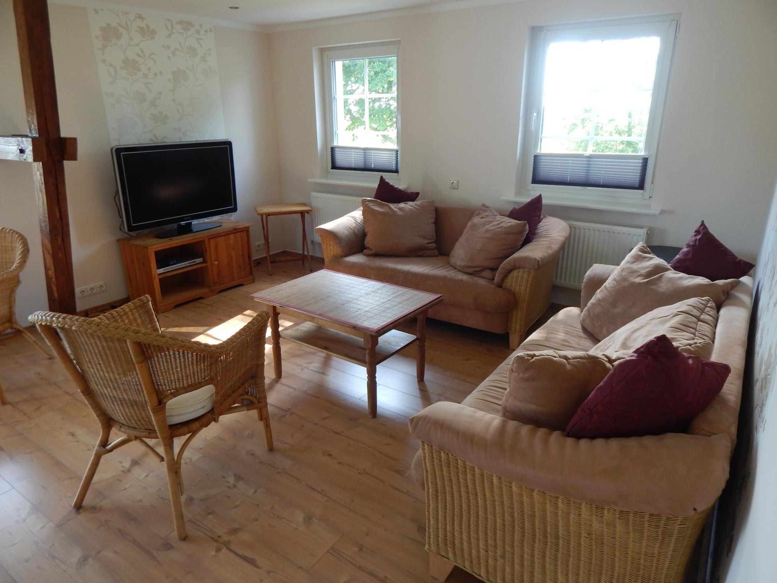 A living room with a television, two sofas, a coffee table, and wicker chairs.