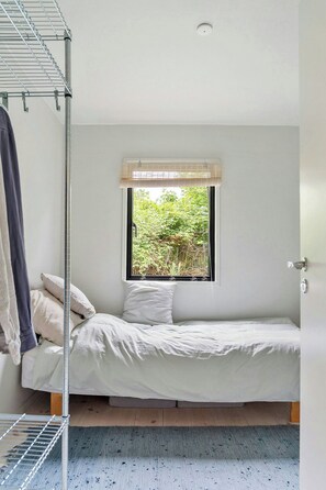 Ein kleines Zimmer mit einem Einzelbett, einem Fenster mit Blick auf Grünflächen, einem Heizkörper und einer Tür.