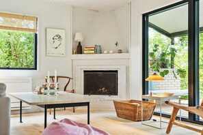 Ein gemütliches Wohnzimmer mit Kamin, einem Esstisch und einem großen Fenster mit Blick auf Grünflächen.