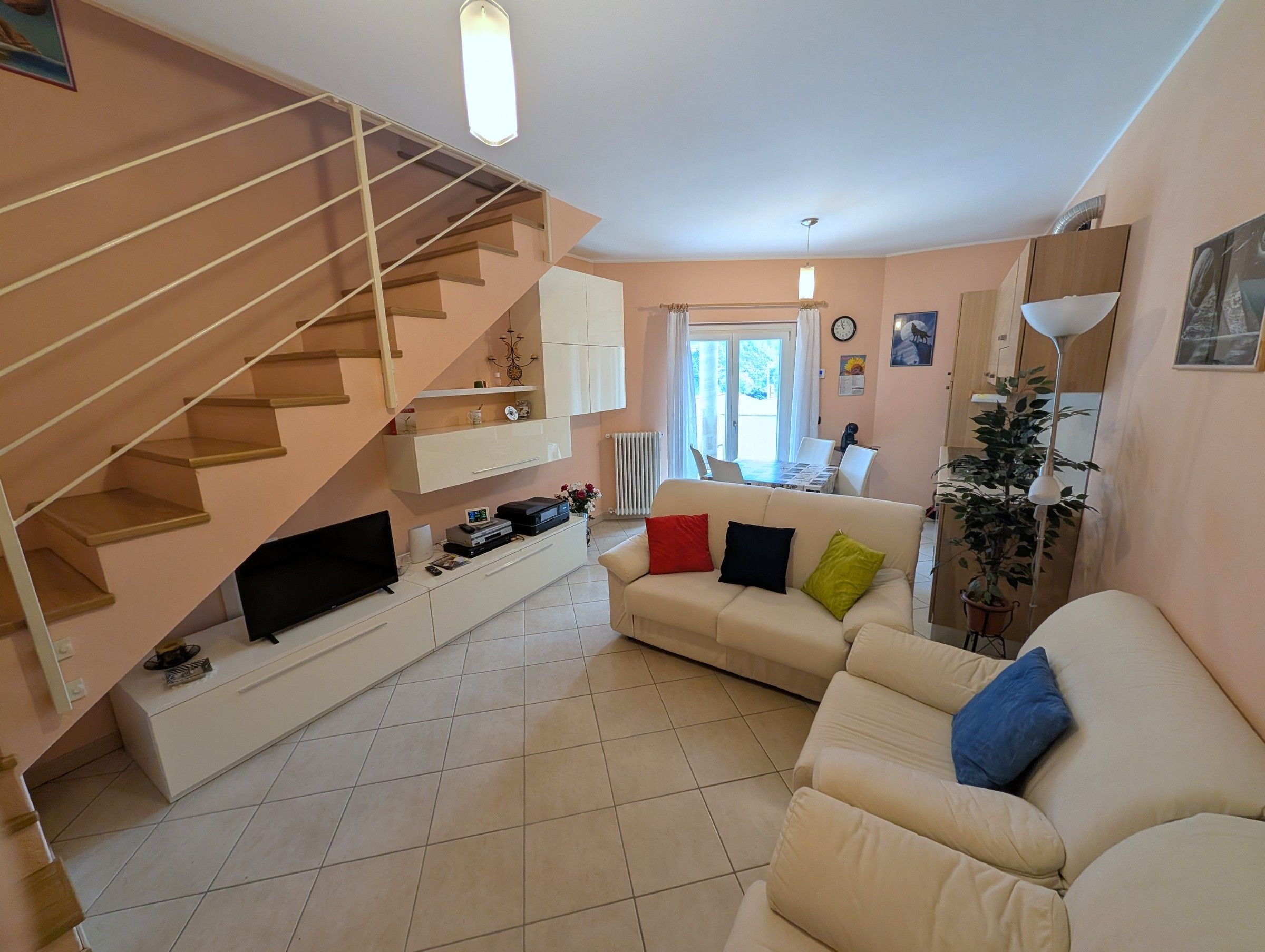 A living room with a staircase, a sofa, a dining table, and a radiator.