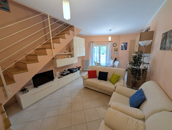 A living room with a staircase, a sofa, a dining table, and a radiator.