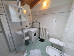 Un baño compacto con cabina de ducha de vidrio, lavadora, radiador y retrete.