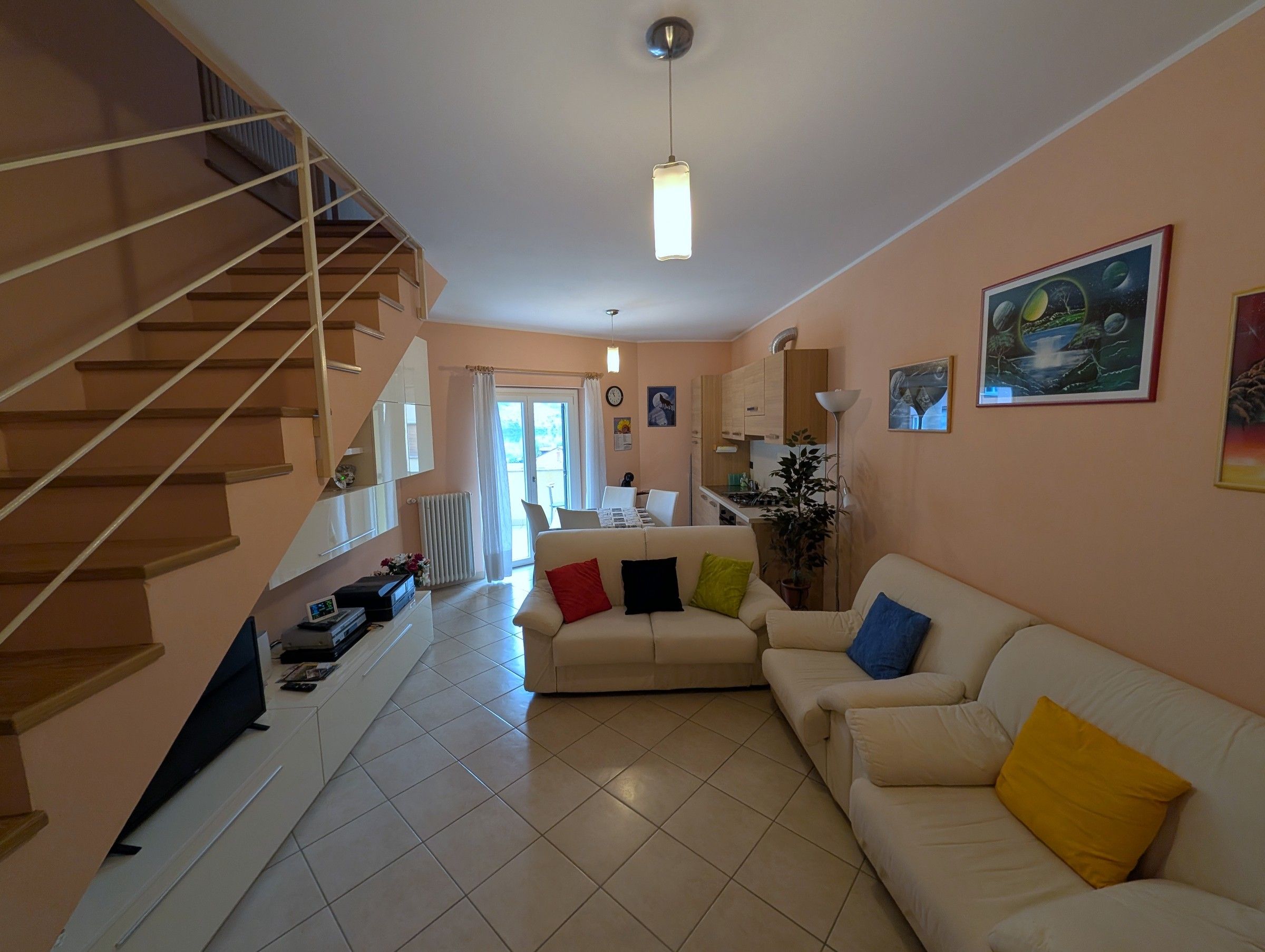 A living room with a staircase, a sofa set, a dining area, and a kitchen.