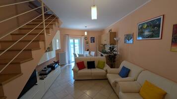 A living room with a staircase, a sofa set, a dining area, and a kitchen.