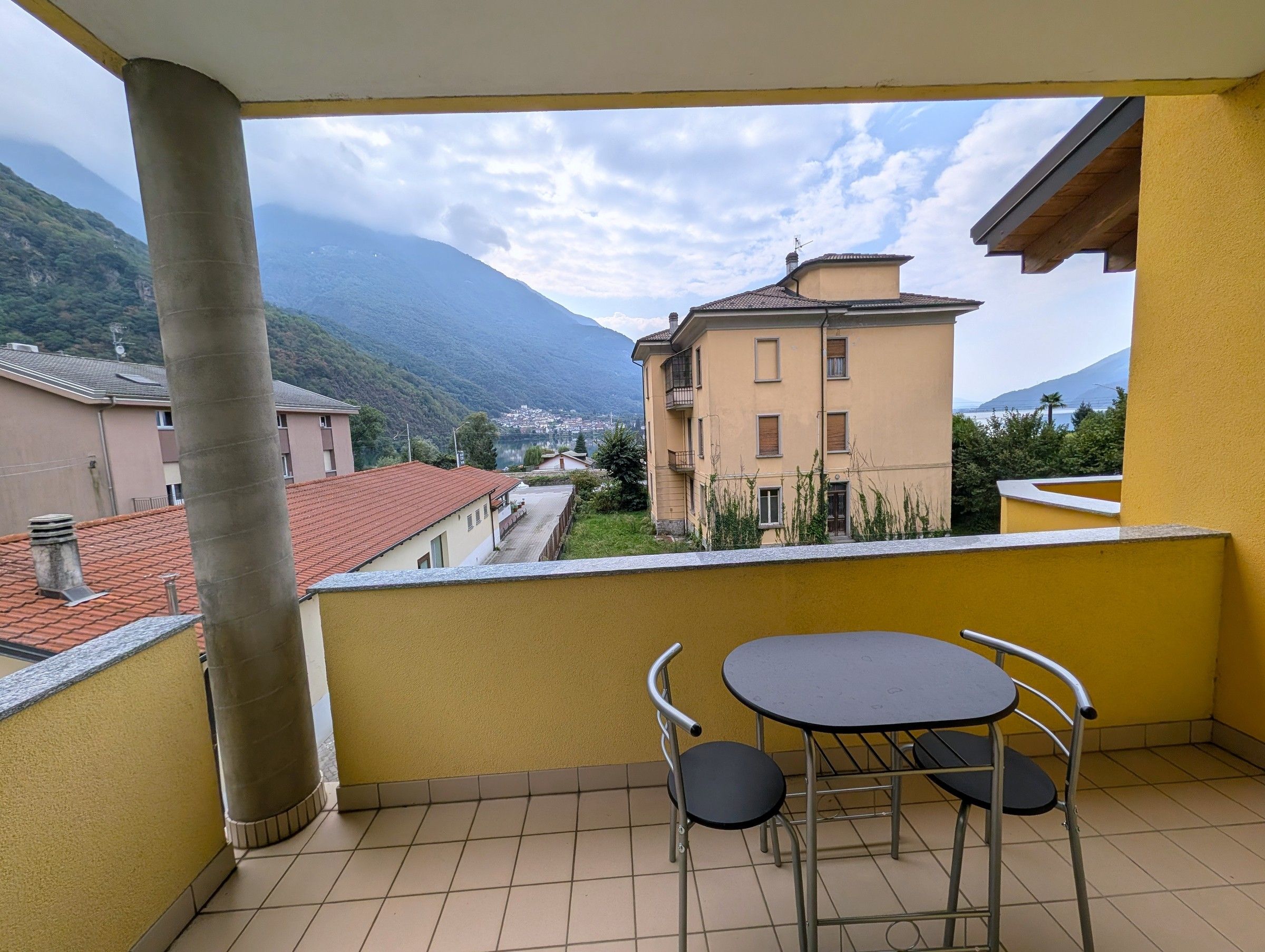Ein Balkon mit Tisch und Stühlen, der auf einen Wohnbereich mit Gebäuden und einem Berg Blick bietet.