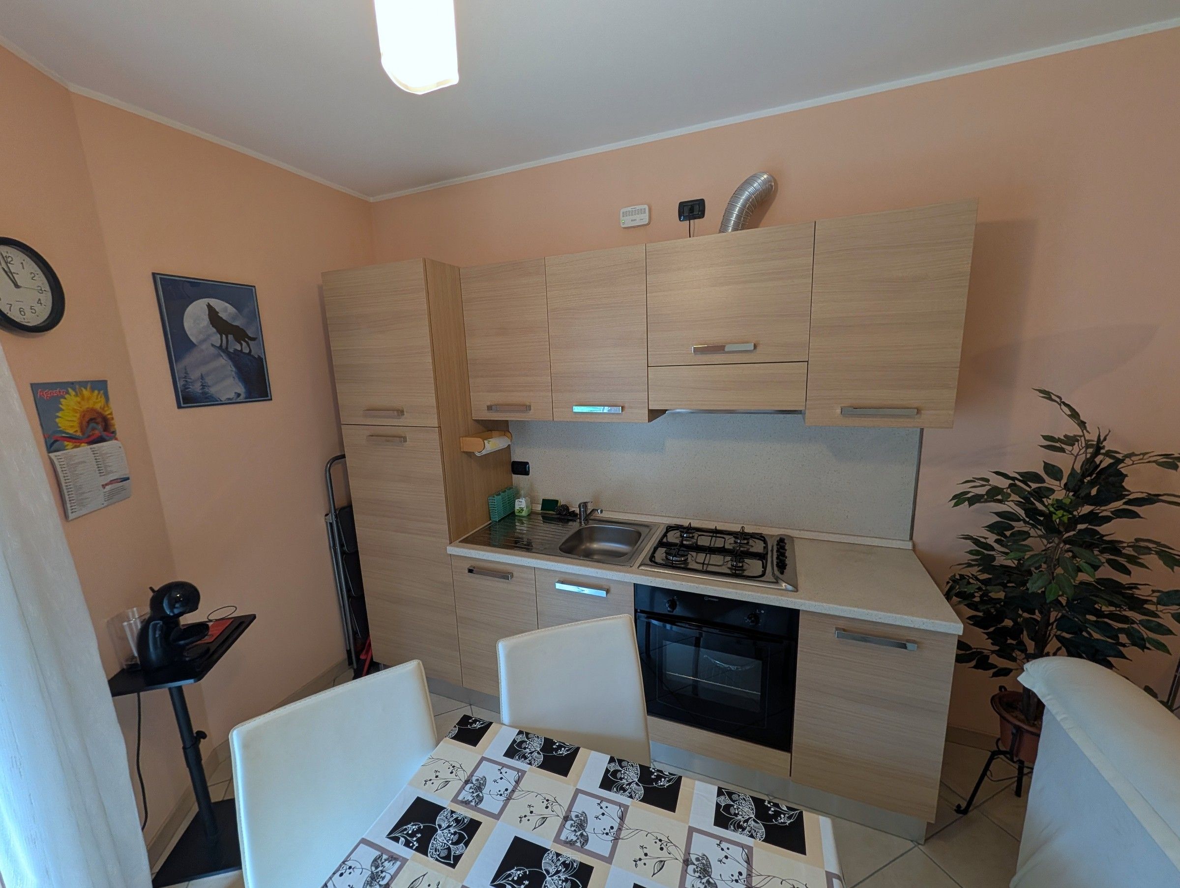 Une cuisine compacte équipée d’une cuisinière à gaz, d’un four et d’un évier. Un petit coin repas avec une table et des chaises est également disponible.
