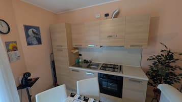Cocina compacta con estufa a gas, horno y lavamanos. Cuenta con un pequeño comedor con mesa y sillas.