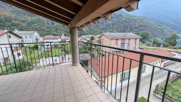 Un balcón con suelo de baldosas, techo de madera y vista a una zona residencial con casas y una montaña al fondo.