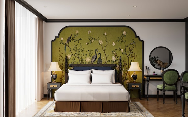 Habitación de hotel con una cama grande, dos mesitas de noche con lámparas, una silla verde y un espejo redondo sobre una cómoda.