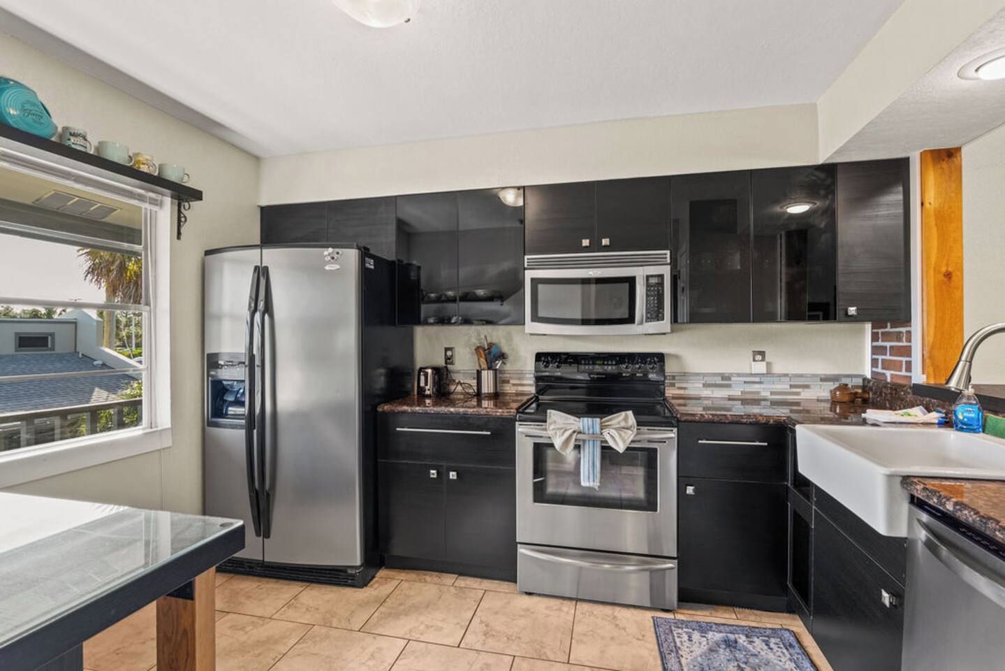 A modern kitchen with stainless steel appliances, black cabinetry, and a window overlooking a residential area.