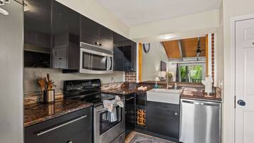 Une cuisine moderne dotée d’appareils électroménagers en acier inoxydable, de meubles de rangement aux couleurs sombres et d’un plan de travail en bois.