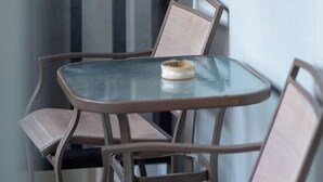 Una mesa con cubierta de vidrio y cuatro sillas, una mesa redonda pequeña con un plato, y una ventana con persianas.