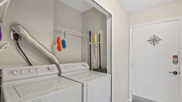 Ett tvättrum med två tvättmaskiner och två torktumlare staplade ovanpå varandra, en ventilationsslang och en dörr med en kompassymbol.